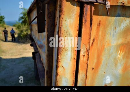 Bulgarien und Aussicht von niedlichen und kleinen Dörfern während hellen Tag. Abgenutzt und alt ein Traktor Anhänger und zwei Männer zu Fuß und verschwommen Hintergrund. Stockfoto