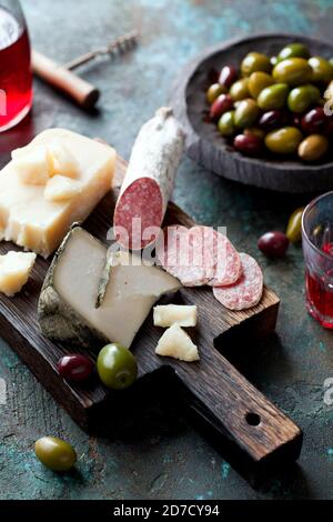 Antipasto-Tafel mit geschnittener Salami, Ziegenkäse, sortierten Oliven und Rotwein, selektiver Fokus Stockfoto