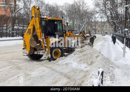 Sankt Petersburg, Russland - 06. Februar 2018: Gelber Traktor JCB nach Schneefall räumt an einem düsteren Wintertag die Straße und die Straße Stockfoto