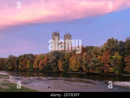 22. Oktober 2020, Bayern, München: Bei Sonnenaufgang über der Isar erscheint ein bunter Himmel. Im Hintergrund ist die katholische Pfarrkirche St. Maximilian zu sehen. Foto: Christian Kunz/dpa Stockfoto