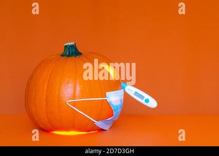 Seitenansicht Halloween Kürbis Kopf Jack Laterne trägt medizinische Maske das Thermometer ist in der Nase, auf trendigen orangen Tisch Hintergrund kopieren Raum Banner A Stockfoto