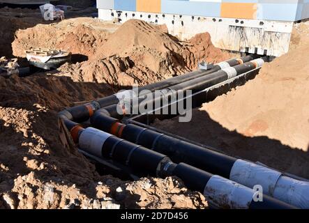 Verlegung von Heizrohren in einem Graben auf der Baustelle. Installation von unterirdischen Sturmsystemen für die Wasserleitung und die Sanitärabwasserkanäle Kaltes und warmes Wasser, Heizung Stockfoto
