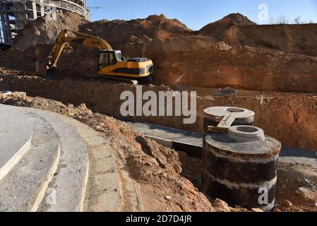 Bagger auf Erdarbeiten während der Verlegung der Rohre der Heizungsanlage zu einem neuen Wohngebäude auf der Baustelle. Verlegung von Betonabwasserkanälen Stockfoto