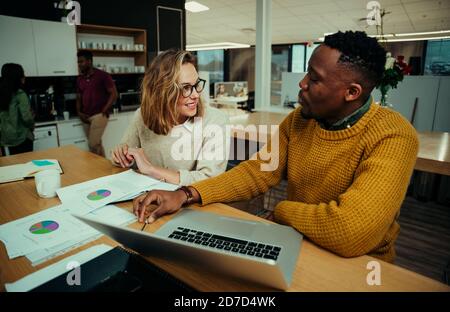 Junge Unternehmer arbeiten im Büro analysieren Tortendiagramme und Recherche Auf dem Laptop, während Kollegen bei einer Tasse Kaffee plaudern Stockfoto