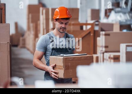 Arbeiter in orange hart hatte ist im Lager mit Box in den Händen Stockfoto