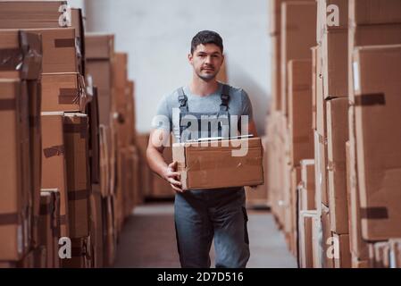 Junge männliche Arbeiter in Uniform ist im Lager mit Box in den Händen Stockfoto