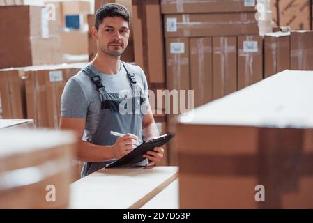 Lagerarbeiter in Uniform und Notizblock in Händen kontrolliert die Produktion Stockfoto