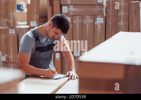 Lagerarbeiter in Uniform und Notizblock in Händen kontrolliert die Produktion Stockfoto