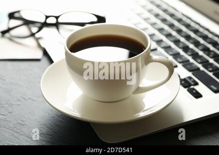 Laptop, Gläser und Tasse Kaffee auf schwarzem Tisch Stockfoto