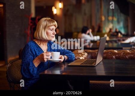Porträt einer älteren Frau, die drinnen im Café sitzt Mit modernem Laptop Stockfoto