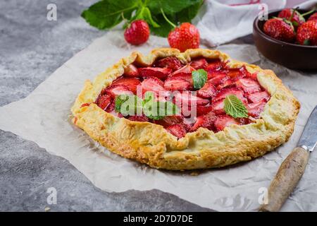 Galette mit Erdbeere auf dem grauen Betonsteingrund. Vegetarische, gesunde Beerentarte, dekoriert mit frisch geschnittenen Erdbeeren und Minze. Delikatesse Stockfoto