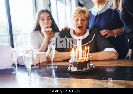 Kerzen blasen. Ältere Frau mit Familie und Freunden feiern einen Geburtstag im Haus Stockfoto