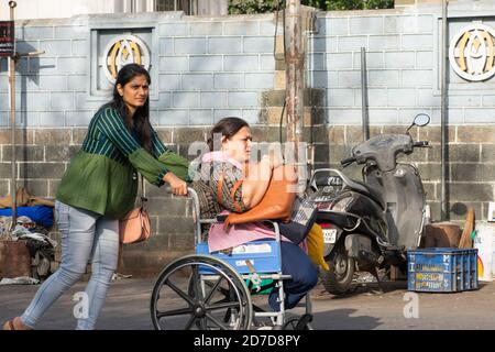 Mumbai, Indien - 22. März 2019: Junge Frau in legerer Kleidung, die den Rollstuhl einer körperlich behinderten Frau schiebt, die am Mount Mary, Bandra, gesichtet wurde. Stockfoto