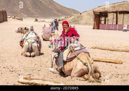 Hurghada, Ägypten - 1. Oktober 2020: Ein junges ägyptisches Mädchen in einem bunten Kleid sitzt auf ihrem Kamel in Hurghada, Ägypten Stockfoto