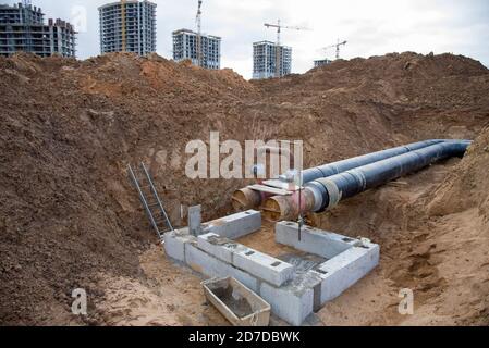 Verlegung von Heizrohren in einem Graben auf der Baustelle. Installation unterirdischer Sturmabwasserkanäle von Wasserleitung und Sanitärkanal auf dem Hintergrund Turm Stockfoto