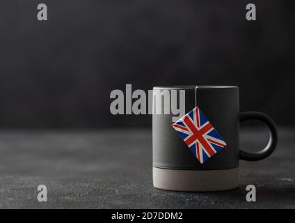 Teebeutel mit Flagge von Großbritannien in grauer Keramik-Tasse auf dunklem Hintergrund. Nachmittagstee Tradition Stockfoto