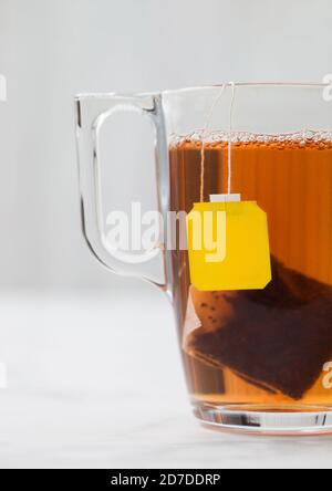 Gelbes Label Tag schwarzer Tee Teebeutel in durchsichtiger Glas Tasse auf weißem Hintergrund. Stockfoto