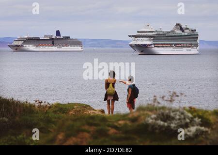 Ein Paar genießt einen Blick auf riesige Kreuzfahrtschiffe vor Torbay in Devon, Großbritannien, ohne Passagiere während der Coronavirus-Pandemie verankert. Hinweis: Die Schiffe sind die Azura und die Arcadia. Beide werden von P&O. betrieben Stockfoto
