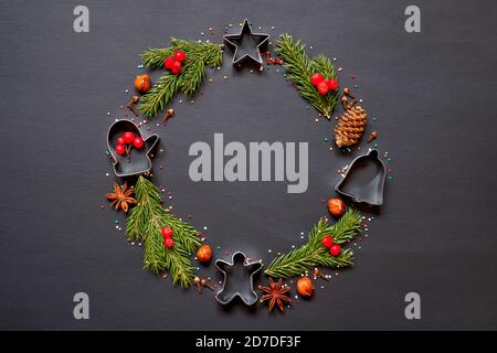 Weihnachtskranz aus Formen für Kekse, Gewürze und einen Weihnachtsbaum auf schwarzem Hintergrund mit Kopierfläche. Stockfoto