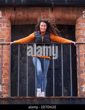Junge Frau mit windgeblasenem Haar auf einem Balkon Stockfoto