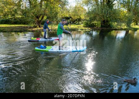 Cambridge, Großbritannien. Oktober 2020. Zwei Männer entspannen sich in der Herbstsonne auf Stand Up Paddle Boards auf der River Cam an einem Tag voller Sonnen, gemischt mit scharfen Duschen. Sie waren gerade in einer schweren Dusche gefangen worden und trockneten jetzt in der Sonne im wechselhaften Herbstwetter aus. Kredit: Julian Eales/Alamy Live Nachrichten Stockfoto