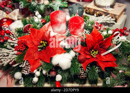 Weihnachtskompositionen und Dekorationen mit Kerzen aus Tannenzweigen, Kugeln und Weihnachtsstern auf dem Jahrmarkt. Stockfoto