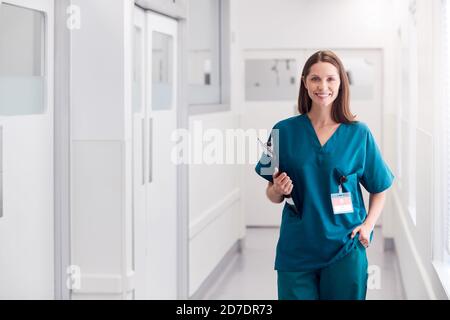 Portrait Von Lächelnder Ärztin, Die Scrubs Trägt, Die Im Krankenhaus Stehen Korridor Mit Zwischenablage Stockfoto