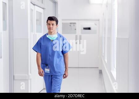 Junge Männliche Arzt Trägt Scrubs Zu Fuß Entlang Krankenhaus Korridor Stockfoto