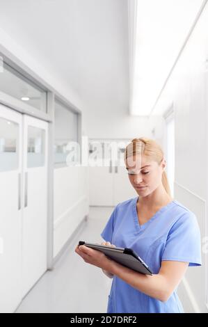 Weibliche Doctor Trägt Scrubs Im Krankenhaus Korridor Mit Digital Tablet Stockfoto