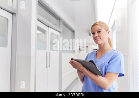 Weibliche Doctor Trägt Scrubs Im Krankenhaus Korridor Mit Digital Tablet Stockfoto
