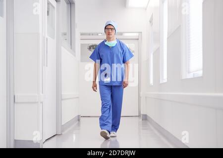 Junge Männliche Arzt Trägt Scrubs Zu Fuß Entlang Krankenhaus Korridor Stockfoto