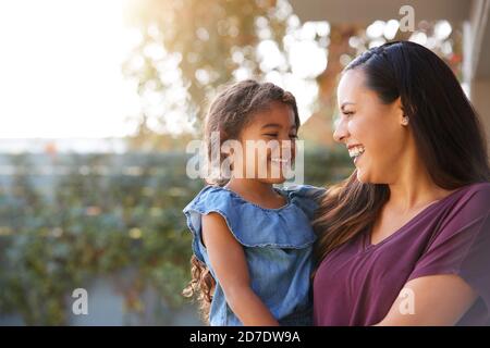 Lächelnd Hispanische Mutter Holding Tochter Lachend Im Garten Zu Hause Stockfoto