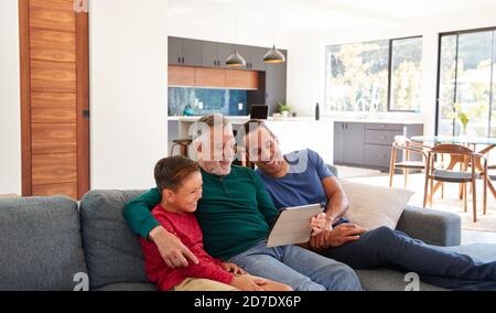 Multi-Generation Männlich Hispanic Familie Sitzt Auf Sofa Zu Hause Beobachten Film Auf Einem Digitalen Tablet Stockfoto
