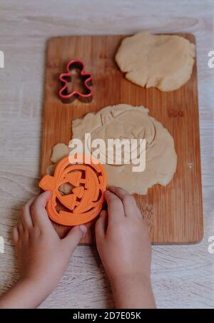 Kleine Kinderhände machen traditionelle Halloween-Kekse. Roher Teig und Ausstecher für die Ferienkekse auf Holztischuntergrund. Cookies werden vorbereitet Stockfoto