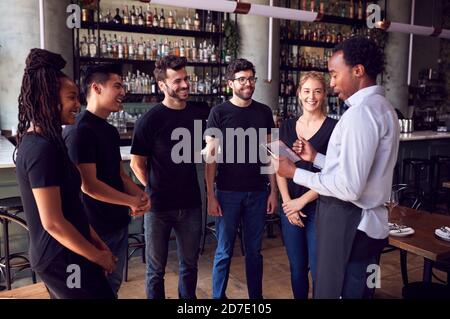 Männlicher Restaurantleiter Mit Digitalem Tablet, Mit Dem Das Team Spricht Bedienungspersonal Stockfoto