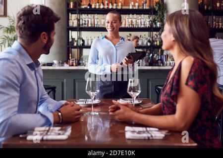 Weibliche Kellnerin Mit Digitalem Tablet Nimmt Auftrag Von Romantischen Paar Sitzen Am Restauranttisch Stockfoto