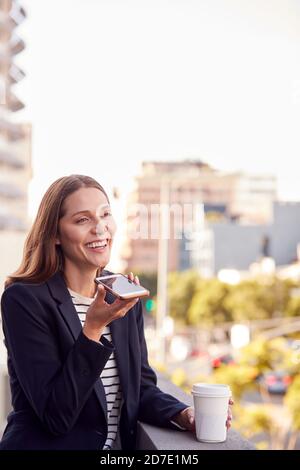 Geschäftsfrau, Die Außerhalb Des Bürogebäudes Mit Mobiltelefon Und Stadt Steht Skyline Im Hintergrund Stockfoto