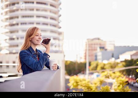 Geschäftsfrau, Die Außerhalb Des Bürogebäudes Mit Mobiltelefon Und Stadt Steht Skyline Im Hintergrund Stockfoto