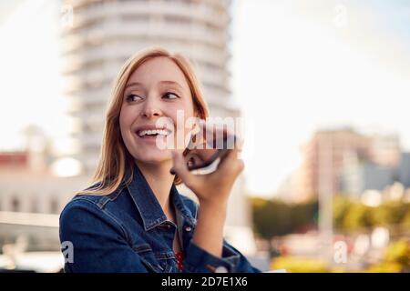 Geschäftsfrau, Die Außerhalb Des Bürogebäudes Mit Mobiltelefon Und Stadt Steht Skyline Im Hintergrund Stockfoto