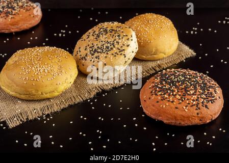 Frisch gebackene Hamburger-Brötchen mit Körnern auf schwarzem Hintergrund Stockfoto