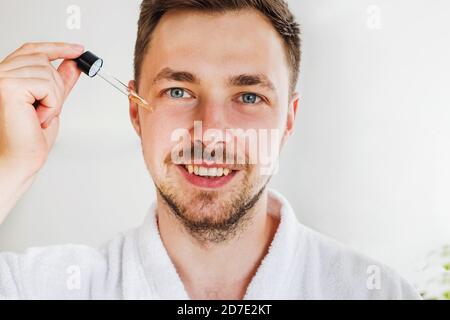 Nahaufnahme von jungen lächelnden schönen Mann gehen, um Serum oder andere Hautpflege-Produkt auf seinem Gesicht gelten. Stockfoto