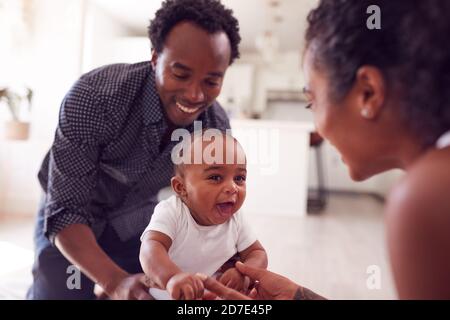 Eltern Ermutigend Lächelnd Baby Tochter Erste Schritte Zu Unternehmen Und Zu Hause Gehen Stockfoto