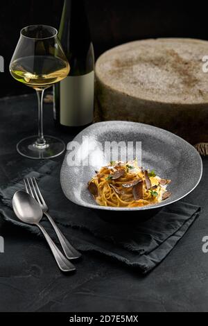 Italienische Küche: Spaghetti mit schwarzem Trüffel auf einem grauen Teller und einer Flasche Wein. Selektiver Fokus. Vertikal. Stockfoto