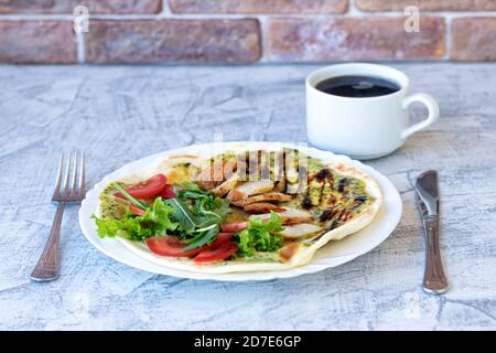 Italienisches Frühstück mit Kaffee. Piadina mit gegrilltem Hähnchen, Tomaten, Salat und Rucola. Köstliches Frühstück auf dem Tisch serviert. Weichfokus Stockfoto