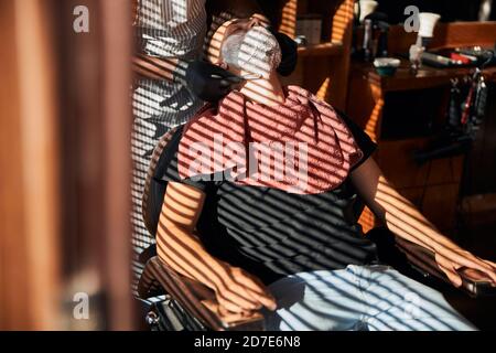 Männliche Barbier in sterilen Handschuhen Rasieren Client Bart im Friseurladen Stockfoto