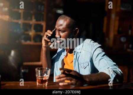 Gutaussehender afroamerikanischer Mann mit Zigarre, die auf dem Handy spricht Stockfoto