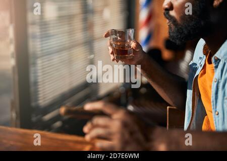 Bärtiger junger Mann, der Zigarre raucht und Whisky trinkt Stockfoto