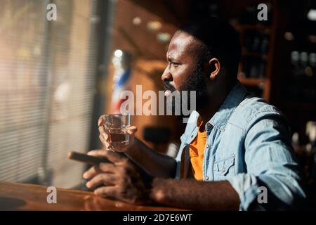 Bärtiger afroamerikanischer Mann, der Zigarre raucht und Whisky trinkt Stockfoto