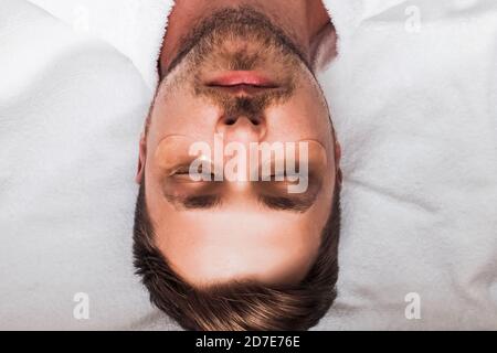 Porträt eines jungen, gutaussehenden Mannes mit Bart liegend und entspannend mit goldenen Flecken unter den Augen. Draufsicht Stockfoto