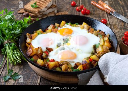 Spiegeleier mit Gemüse - shakshuka in der Pfanne und Roggenbrot auf einem alten hölzernen Hintergrund. Spätes Frühstück. Rustikaler Stil. Mittelöstlicher Tradit Stockfoto